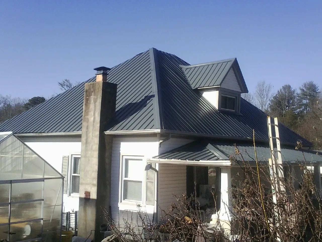 Dark blue standing seam metal roof on a white farmhouse with dormer — Slate & Tile Roof Repair by Roofing Brothers in Queen