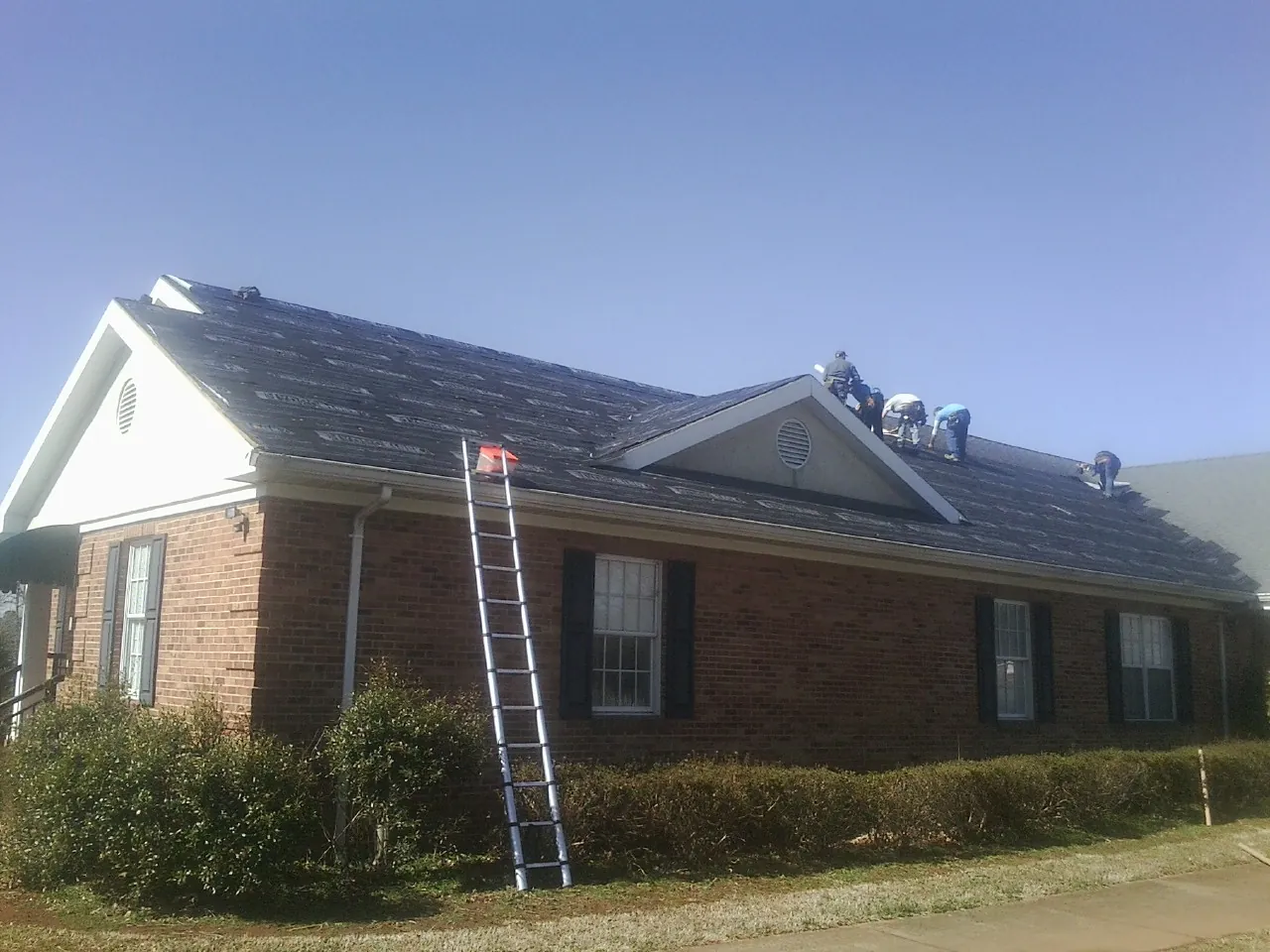 Crew tearing shingles off a brick ranch roof with a ladder set — Metal Roof Repair work by our crew in Queen