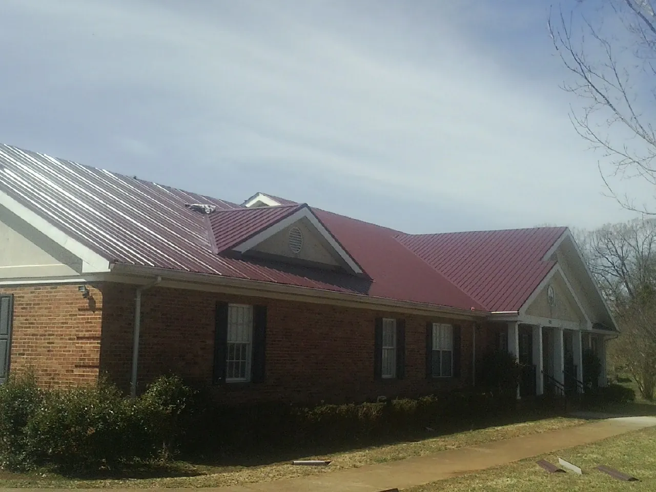 Red metal roof with gabled entries on a long brick building, from a Hail Damage Roof Repair job in Queen