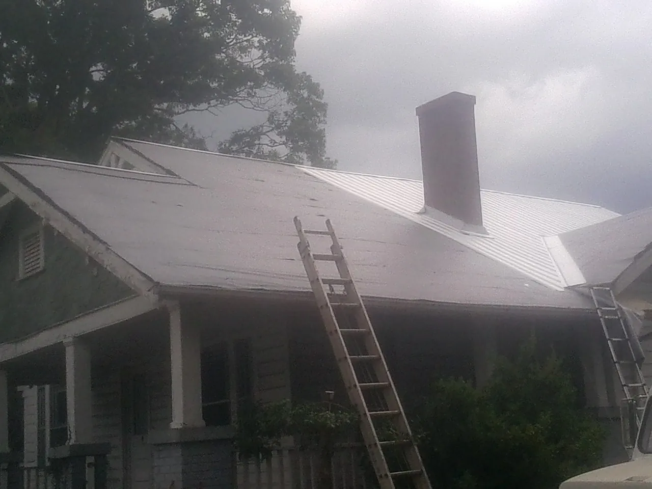 Ladders against a metal roof on an older home with a brick chimney in Queen