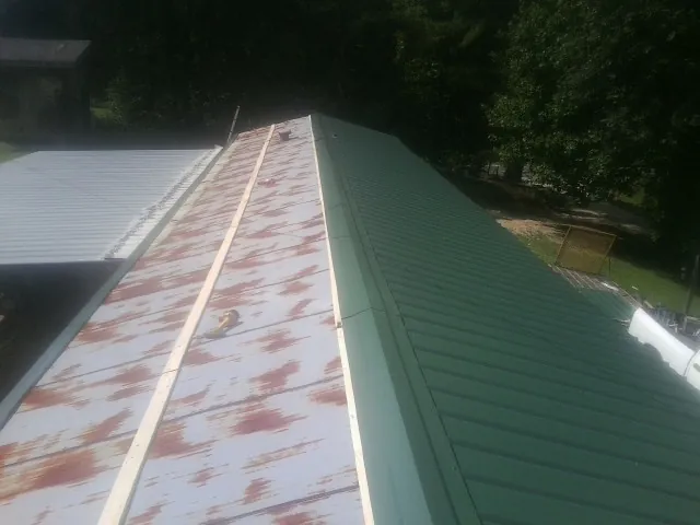 Old rusted panels beside newly installed green metal roofing — Wind Damage Roof Repair by Roofing Brothers in Queen
