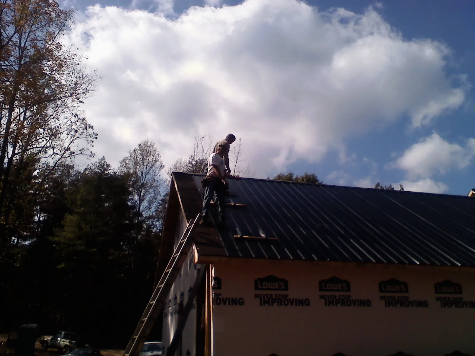 Roofer fastening dark metal panels high against a cloudy sky, from a Roof Inspection job in Queen