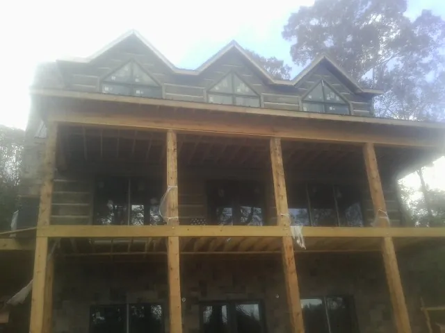 Dormers and porch framing on a large log home under construction — Roof Coating work by our crew in Queen
