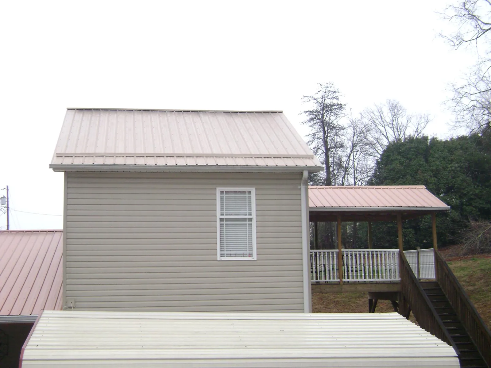 Tan metal roofs on a two story addition and attached porch, from a Roof Replacement job in Queen